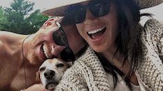 صورة شخصية لهاري وميغان يضحكان في النظارات الشمسية ويعانقان كلبًا أليفًا.