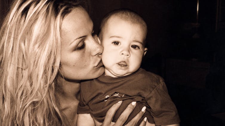 تظهر صورة بني داكن باميلا أندرسون تقبل خد ابنها الرضيع.  لديها شعر أشقر طويل مفترق إلى الجانب.
