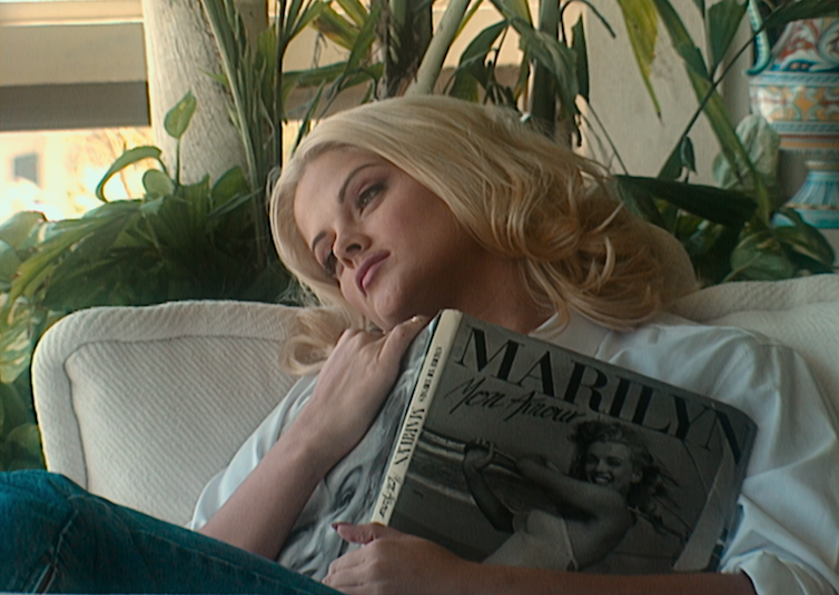 آنا نيكول سميث تتكئ على أريكة ، نسخة من كتاب عن مارلين مونرو مستلقية على صدرها.